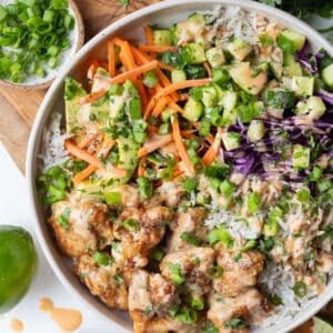 Overhead view of a Bang Bang Chicken Bowl with crispy chicken, rice, carrots, cucumber, and red cabbage next to a small bowl of bang bang sauce.