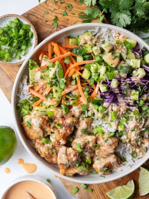 Overhead view of a Bang Bang Chicken Bowl with crispy chicken, rice, carrots, cucumber, and red cabbage next to a small bowl of bang bang sauce.