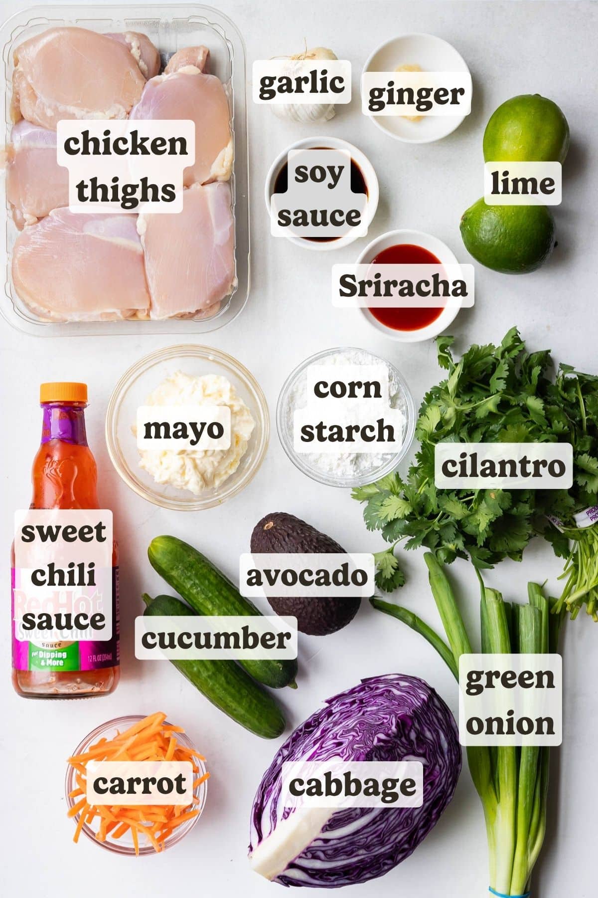 Ingredients for crispy bang bang chicken bowls laid out on a white counter, including chicken thighs, sweet chili sauce, cornstarch, and fresh vegetables.