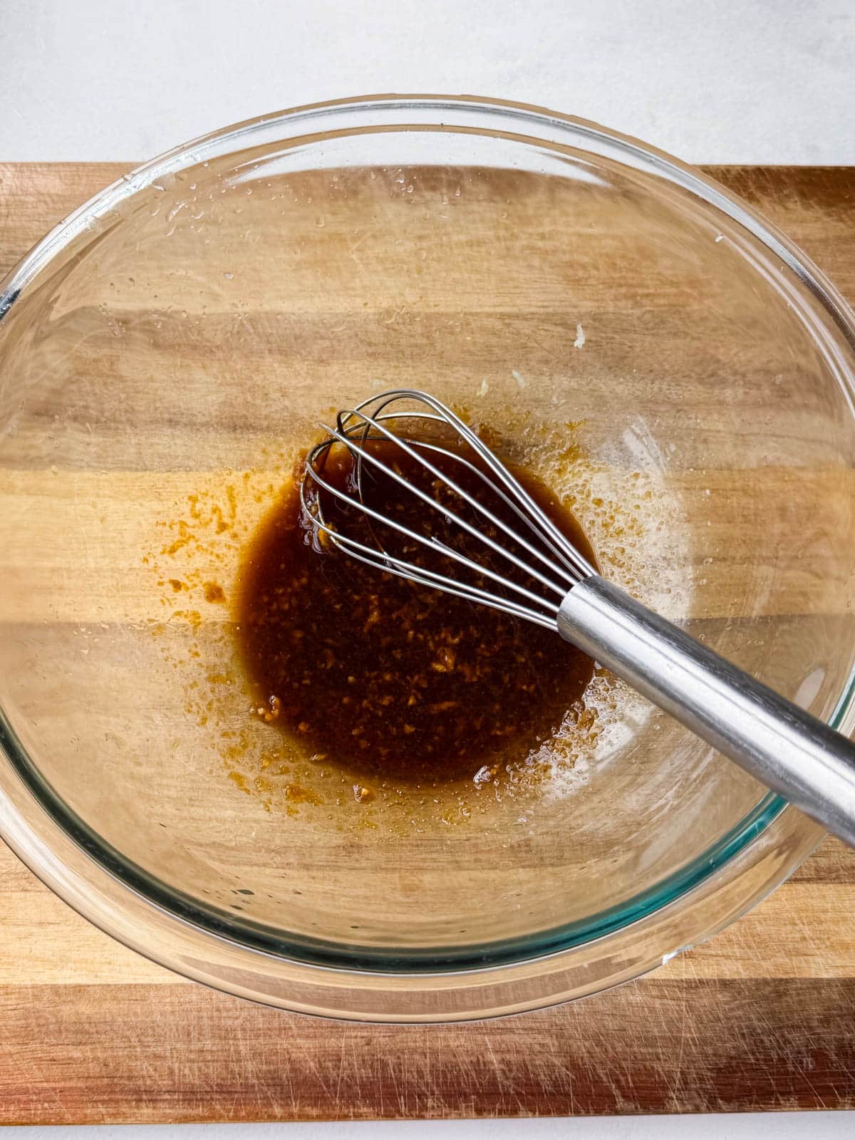 Soy sauce, lime juice, garlic, and ginger whisked together in a glass bowl for the bang bang chicken marinade.