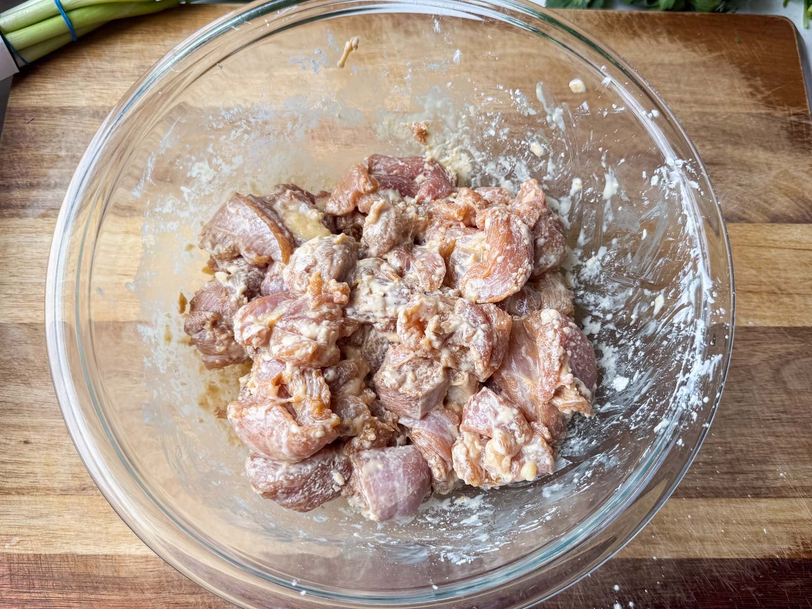 Marinated chicken pieces tossed with cornstarch in a glass bowl before pan-frying.