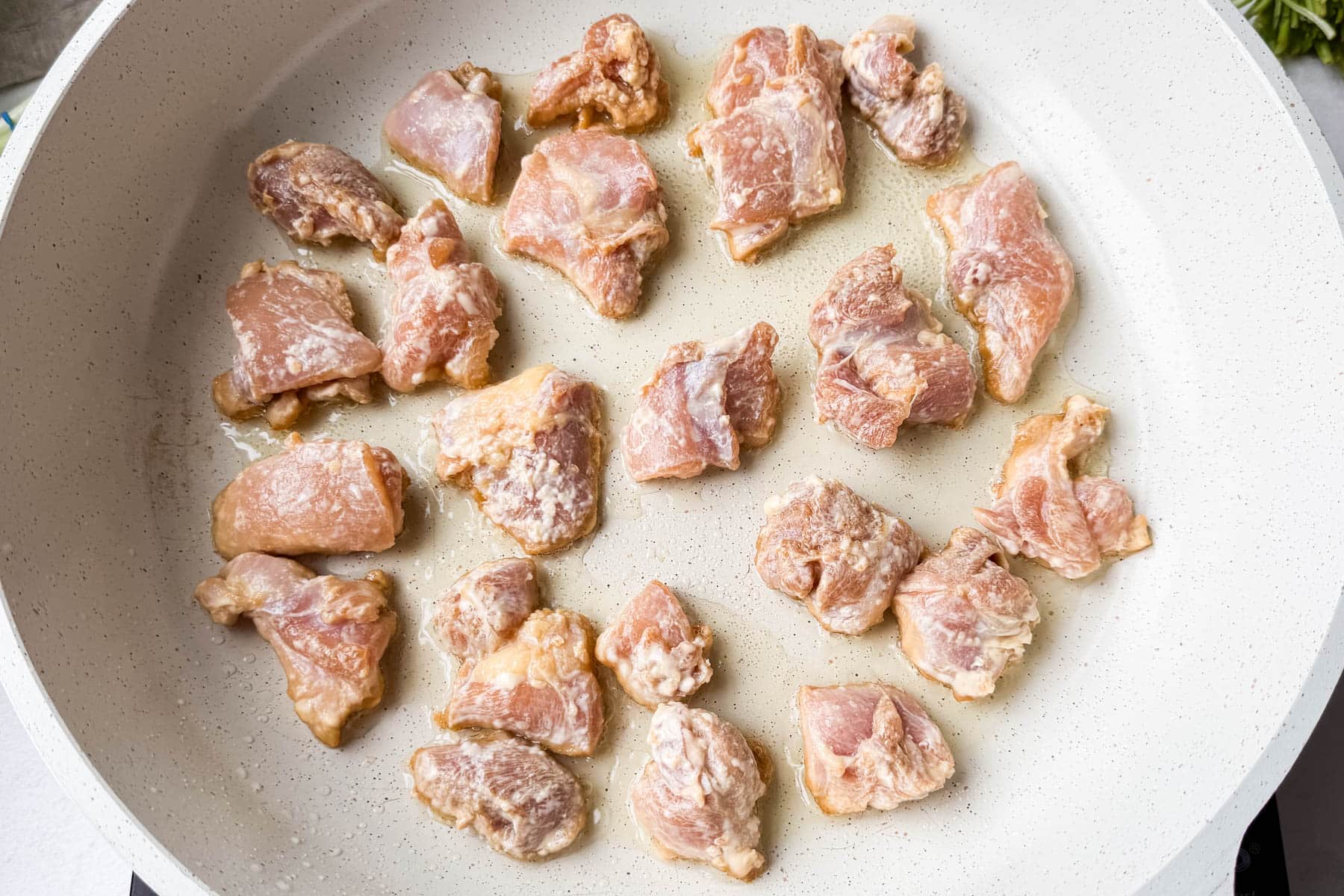 Coated chicken pieces arranged in a single layer in a white skillet.
