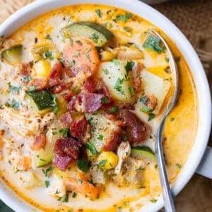 A spoon scoops up a bite of creamy chicken corn chowder with bacon and zucchini.