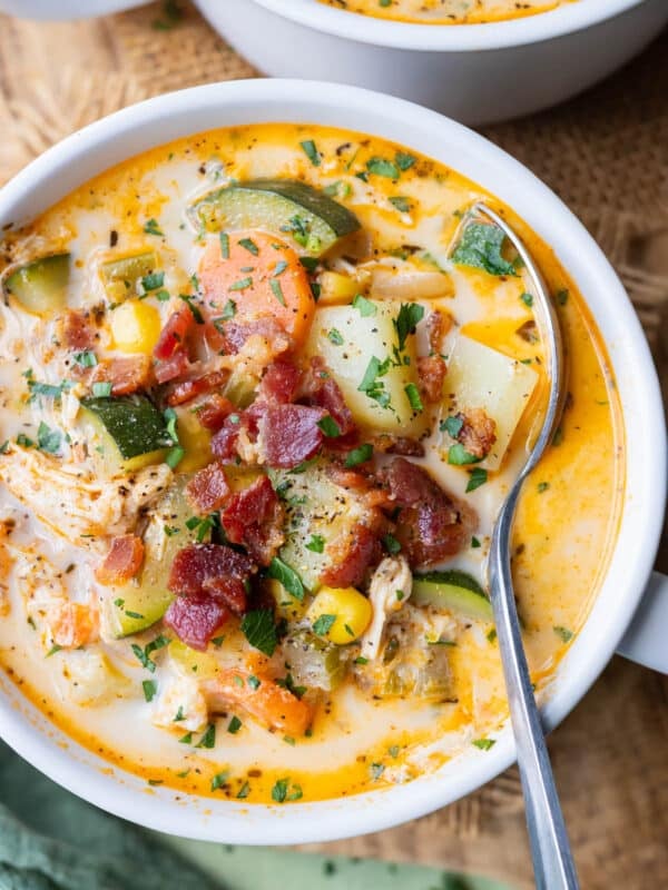 A spoon scoops up a bite of creamy chicken corn chowder with bacon and zucchini.