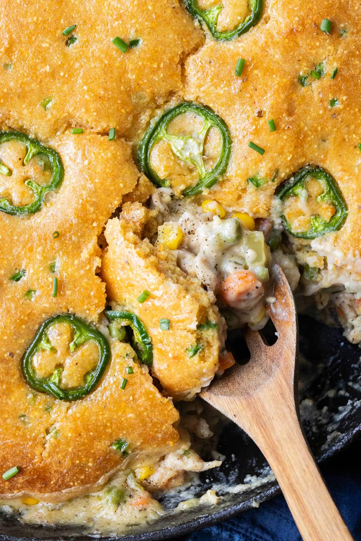 A spoon scoops out a serving of Cornbread Pot Pie from a cast iron skillet
