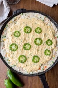 The jalapeno cornbread topping is spread on top of the chicken pot pie filling in one pan.