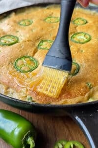 Honey butter is brushed over the top of the cornbread chicken pot pie recipe after baking.
