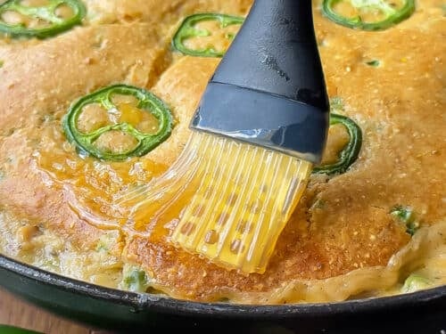 Honey butter is brushed over the top of the cornbread chicken pot pie recipe after baking.