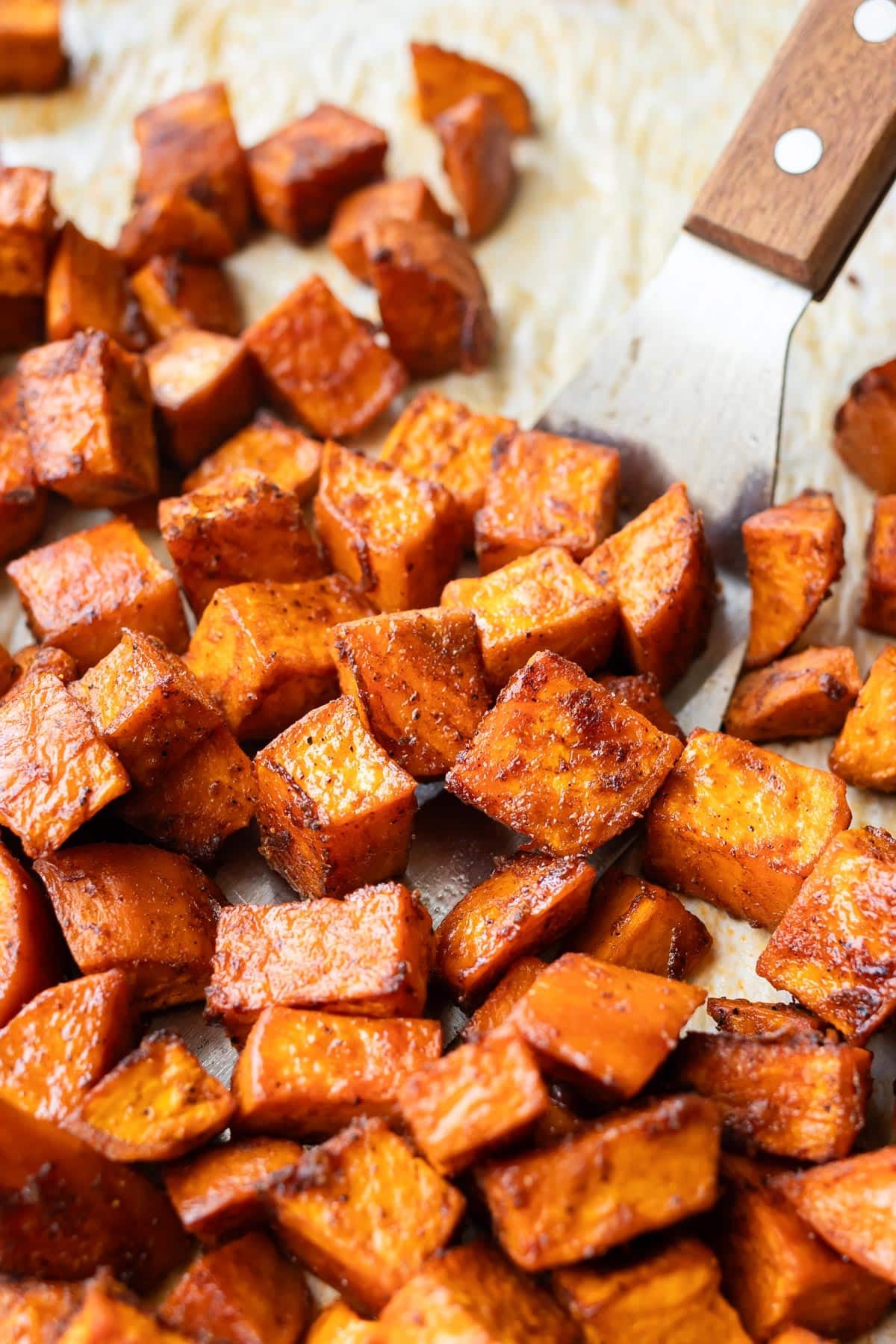 Crispy roasted sweet potato cubes with caramelized edges piled on parchment paper.