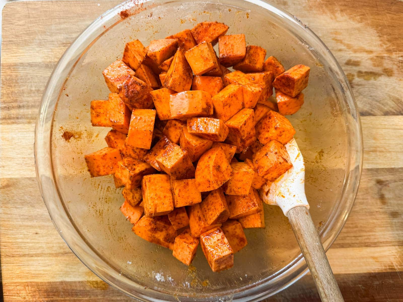 Cubed sweet potatoes are tossed with olive oil and the cornstarch seasoning blend in a glass bowl.