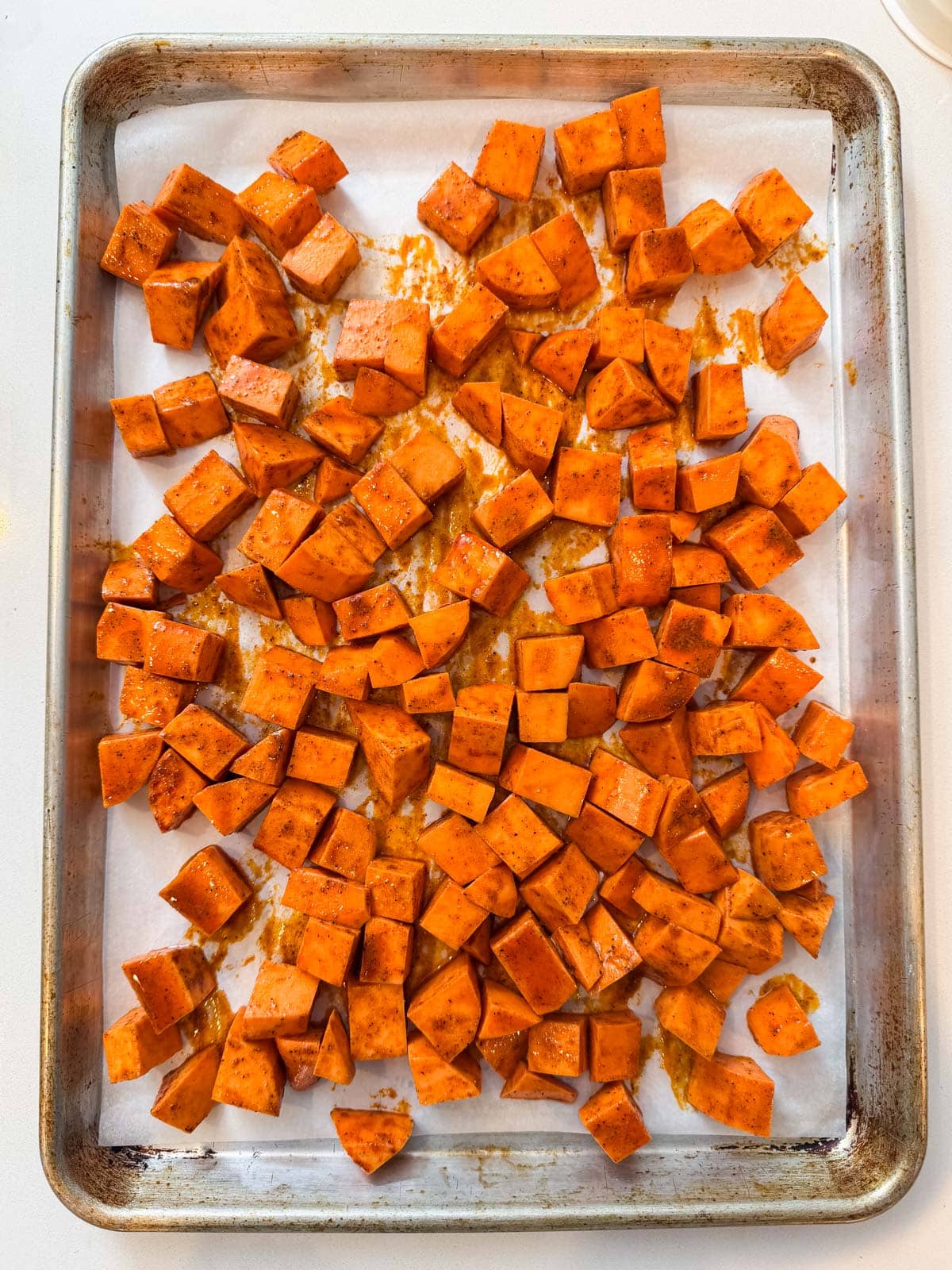 Seasoned sweet potato cubes are spread in a single layer on a parchment-lined sheet pan.