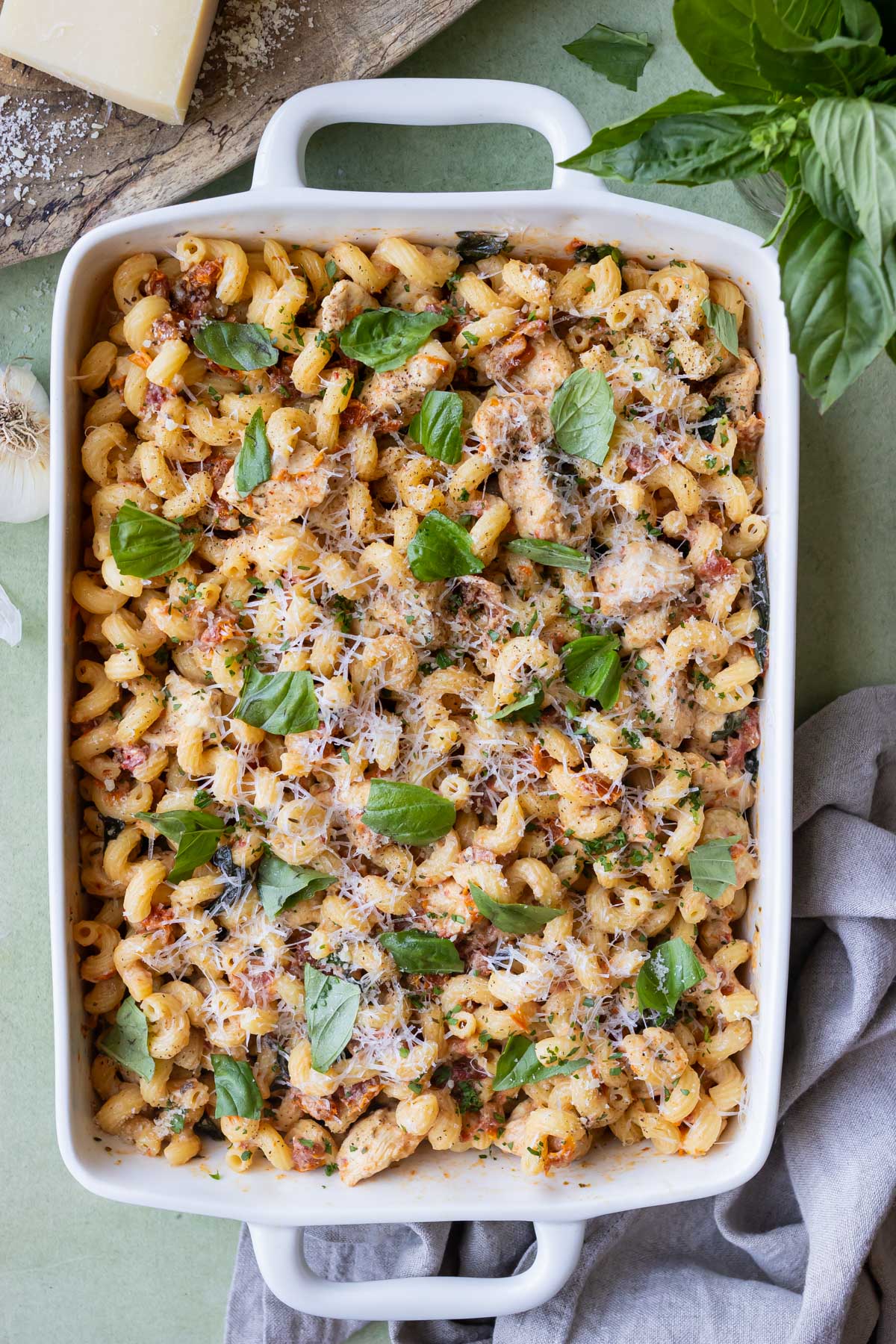 A baking dish is full of a Marry Me Chicken Pasta Dump-and-Bake recipe with sundried tomatoes and a creamy sauce.