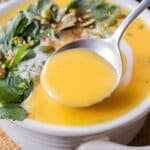 A spoon scoops up some creamy roasted butternut squash soup from a white bowl.