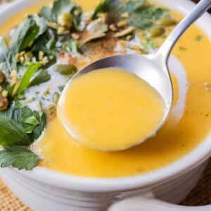 A spoon scoops up some creamy roasted butternut squash soup from a white bowl.