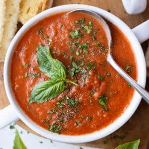 Roasted tomato basil soup in a white bowl topped with a fresh basil leaf and cracked black pepper