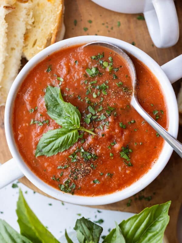 Roasted tomato basil soup in a white bowl topped with a fresh basil leaf and cracked black pepper