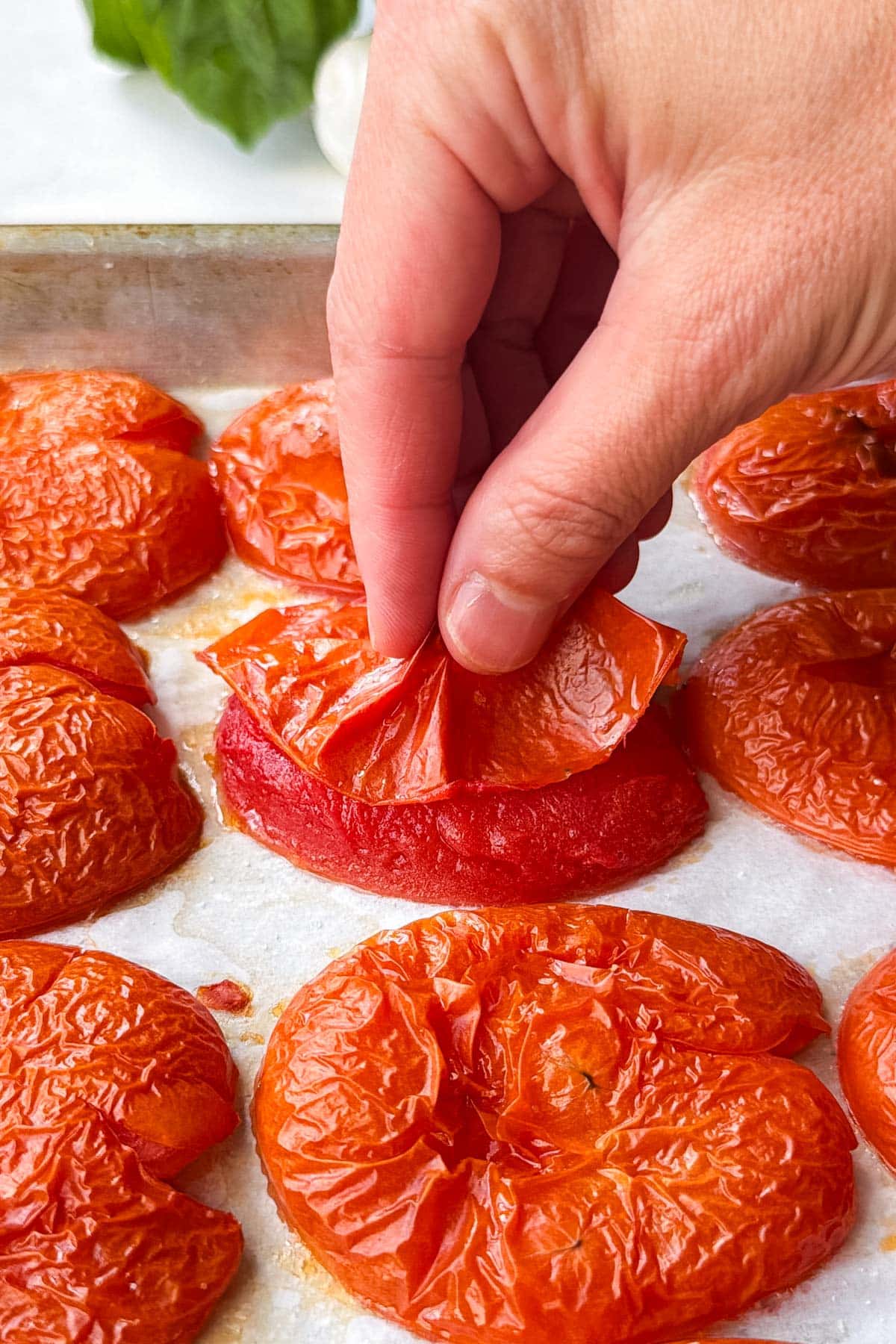 A hand peeling the blistered skin off a roasted tomato