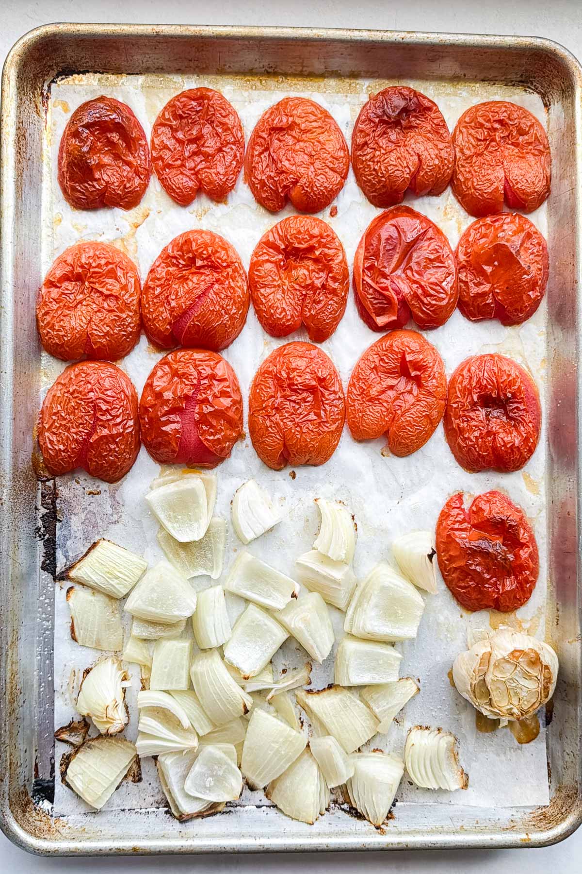 Roasted tomatoes, onion, and a whole head of garlic on a sheet pan straight out of the oven