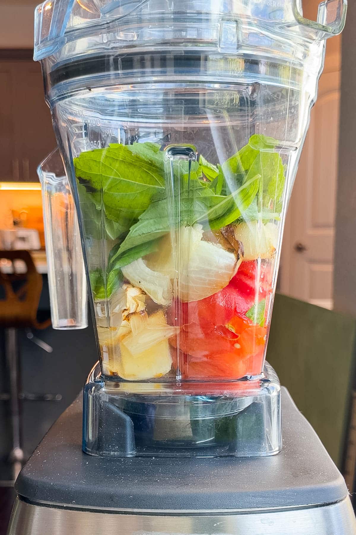 A blender loaded with roasted tomatoes, roasted garlic, onion, and fresh basil leaves before blending