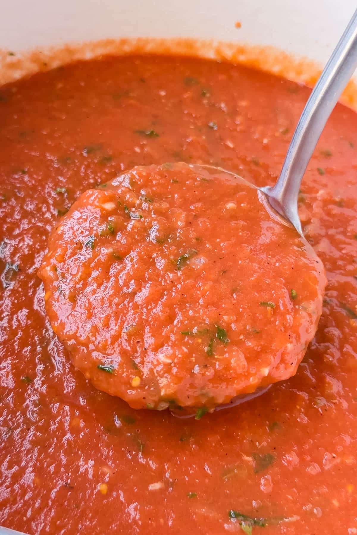 A ladle lifting thick roasted tomato basil soup from the pot