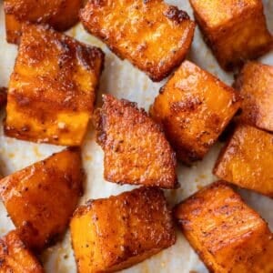 Roasted sweet potato cubes with crispy edges are on a parchment paper lined baking sheet.
