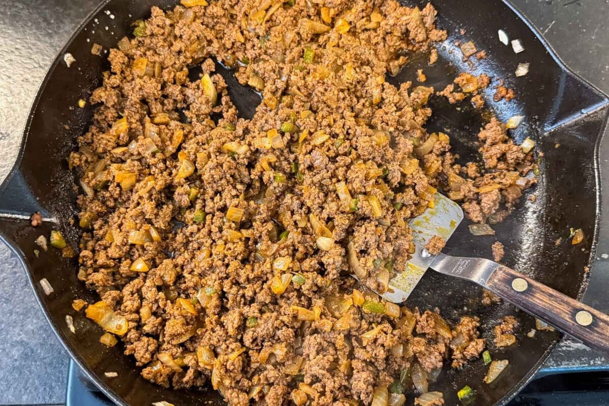 Seasoned ground beef taco meat simmering in a cast iron skillet for sweet potato taco bowls.