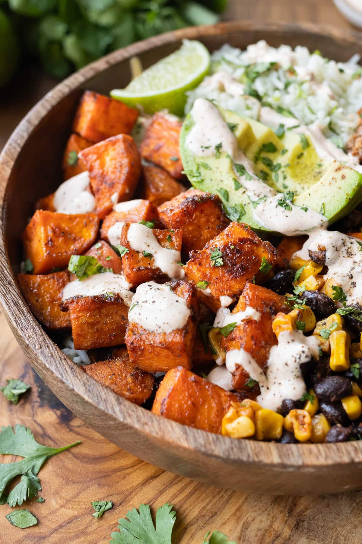 Close-up of a sweet potato taco bowl with crispy roasted sweet potatoes, avocado, black beans, and corn drizzled with chipotle crema.