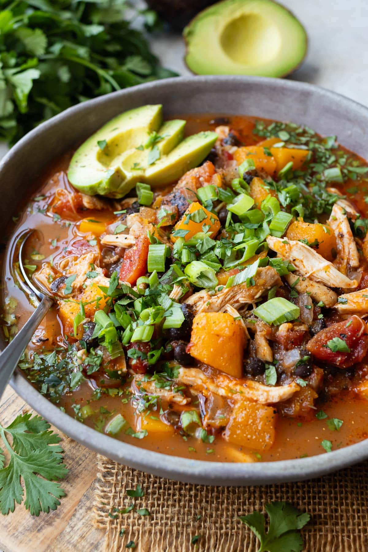 A spoon is scooping up a bite of a chipotle chicken chili with butternut squash from a bowl.