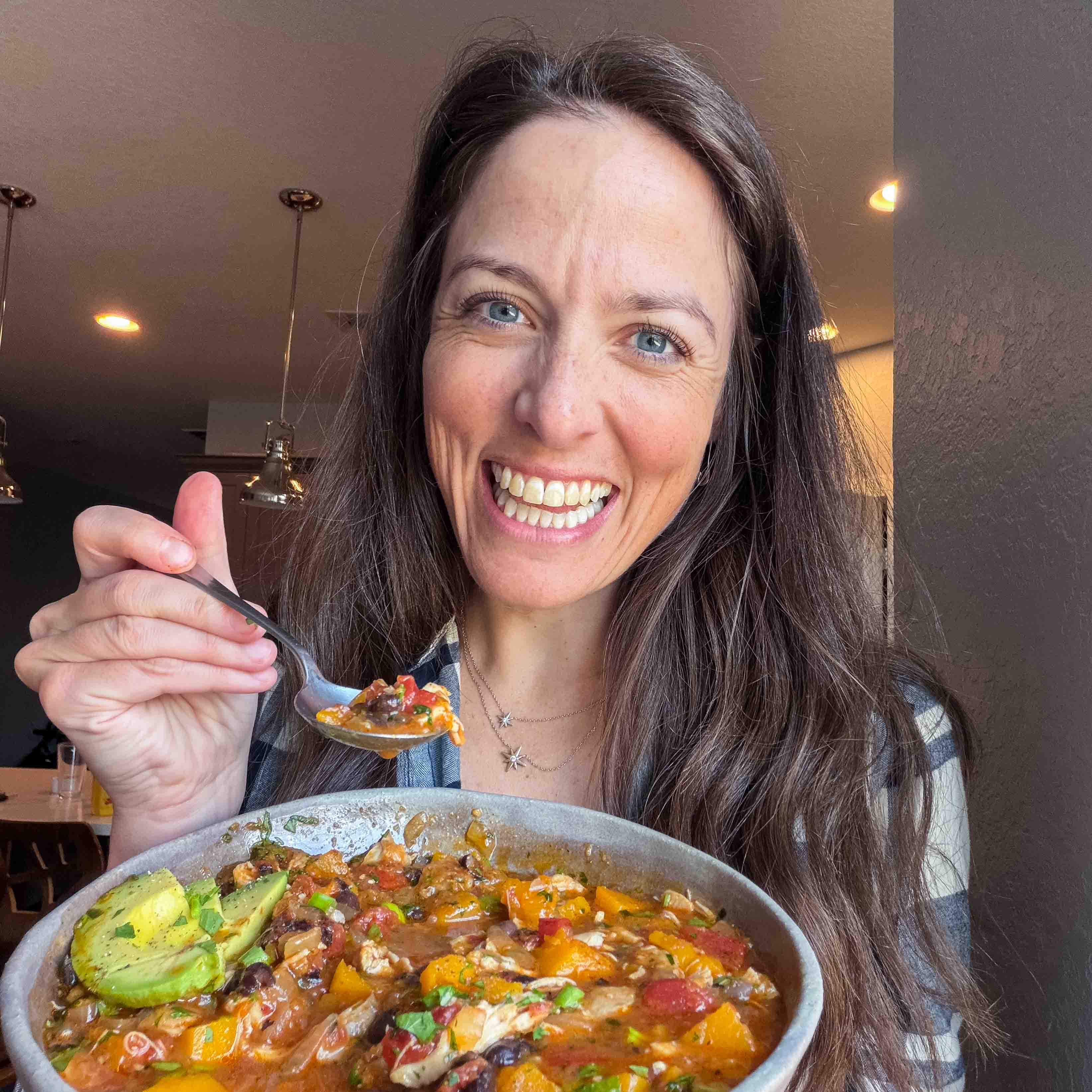 London Lea holding a bowl of chipotle chicken chili with butternut squash in her kitchen.