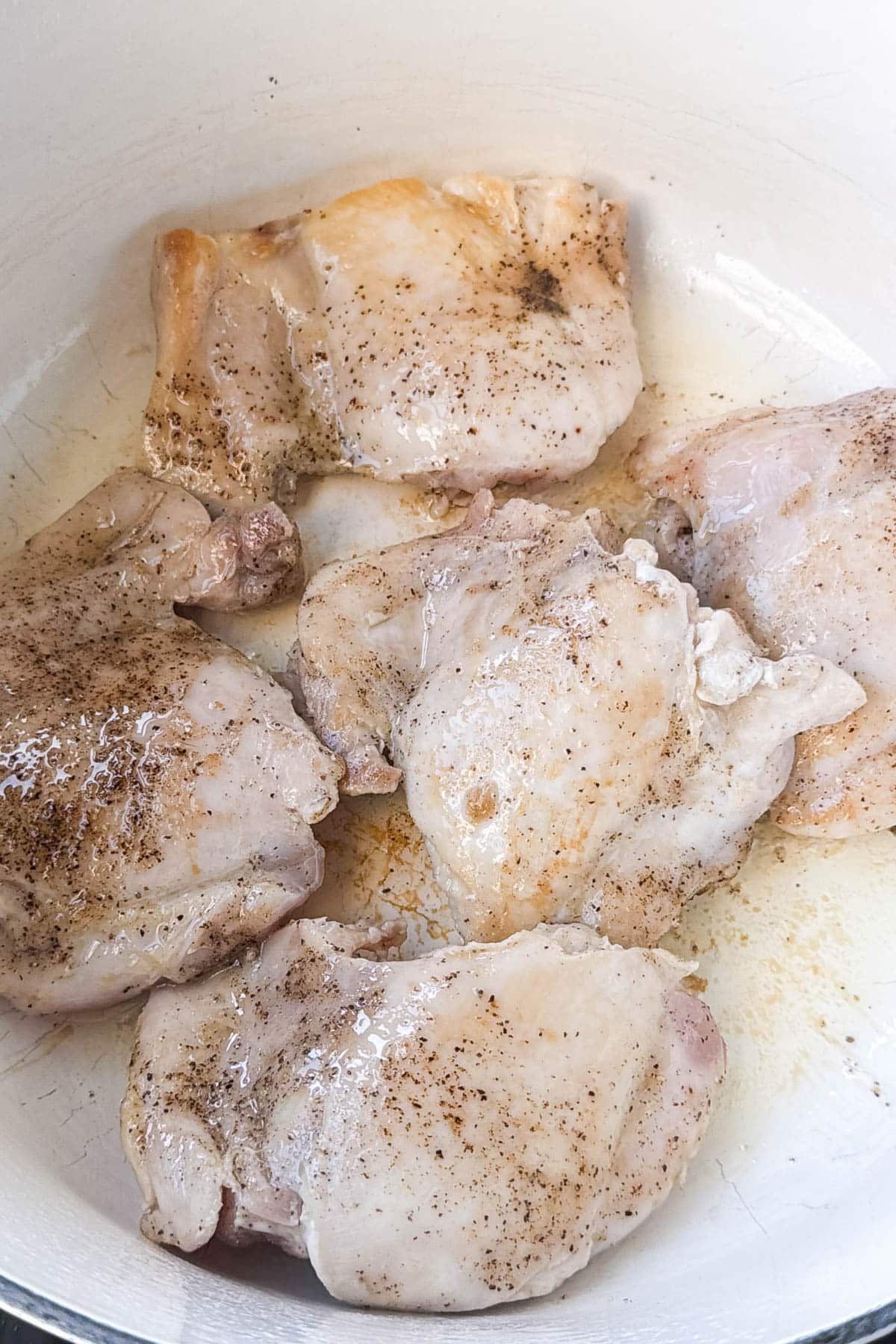 Seasoned chicken thighs searing in a white Dutch oven for chipotle chicken chili
