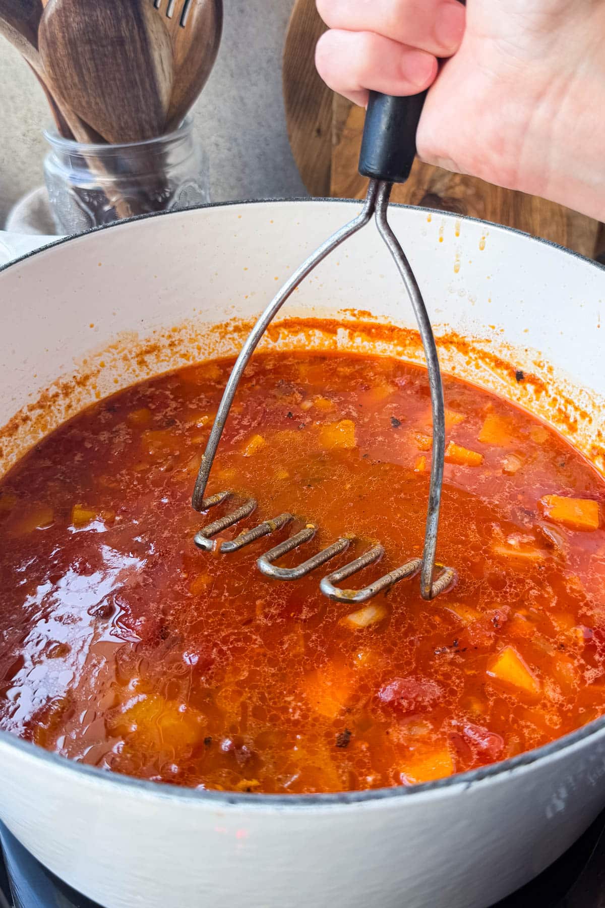 Potato masher pressing butternut squash to thicken chunky chicken chili