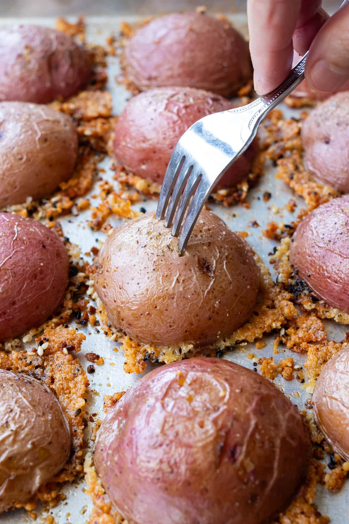 A fork testing a fork-tender parmesan crusted potato on the baking sheet