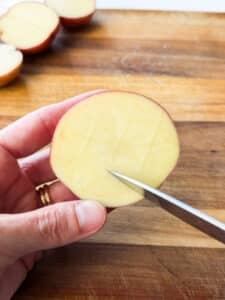 Scoring a tic-tac-toe pattern into a halved red potato for parmesan crusted potatoes