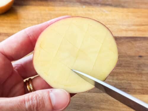 Scoring a tic-tac-toe pattern into a halved red potato for parmesan crusted potatoes