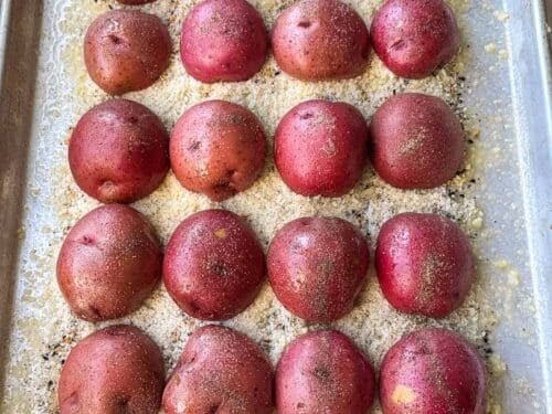 A sheet pan of raw red potato halves cut-side down on everything bagel seasoning and Parmesan