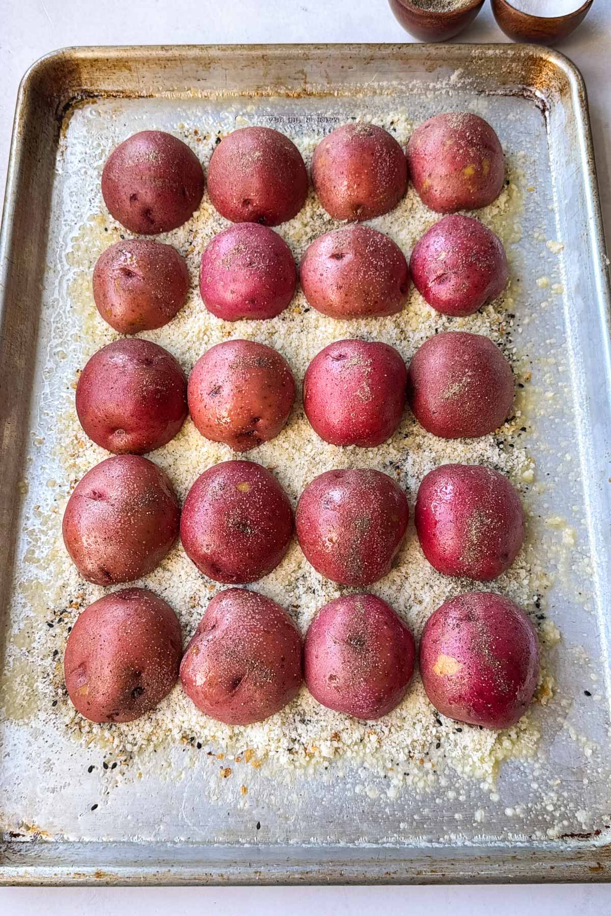 A sheet pan of raw red potato halves cut-side down on everything bagel seasoning and Parmesan