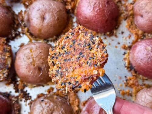 Lifting a crispy parmesan potato off the pan with the everything bagel cheese crust attached