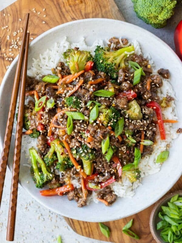 Ground beef and broccoli served over white rice in a bowl with chopsticks and green onions