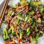 Ground beef and broccoli served over white rice in a bowl with chopsticks and green onions.