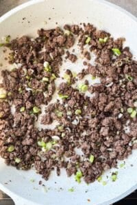 Browned ground beef crumbles with green onions in a nonstick skillet for beef and broccoli stir fry