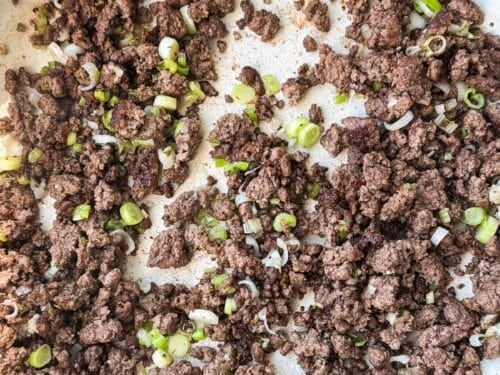 Browned ground beef crumbles with green onions in a nonstick skillet for beef and broccoli stir fry