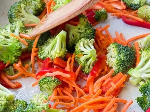 Broccoli florets, matchstick carrots, and red bell pepper cooking in a skillet for ground beef and broccoli