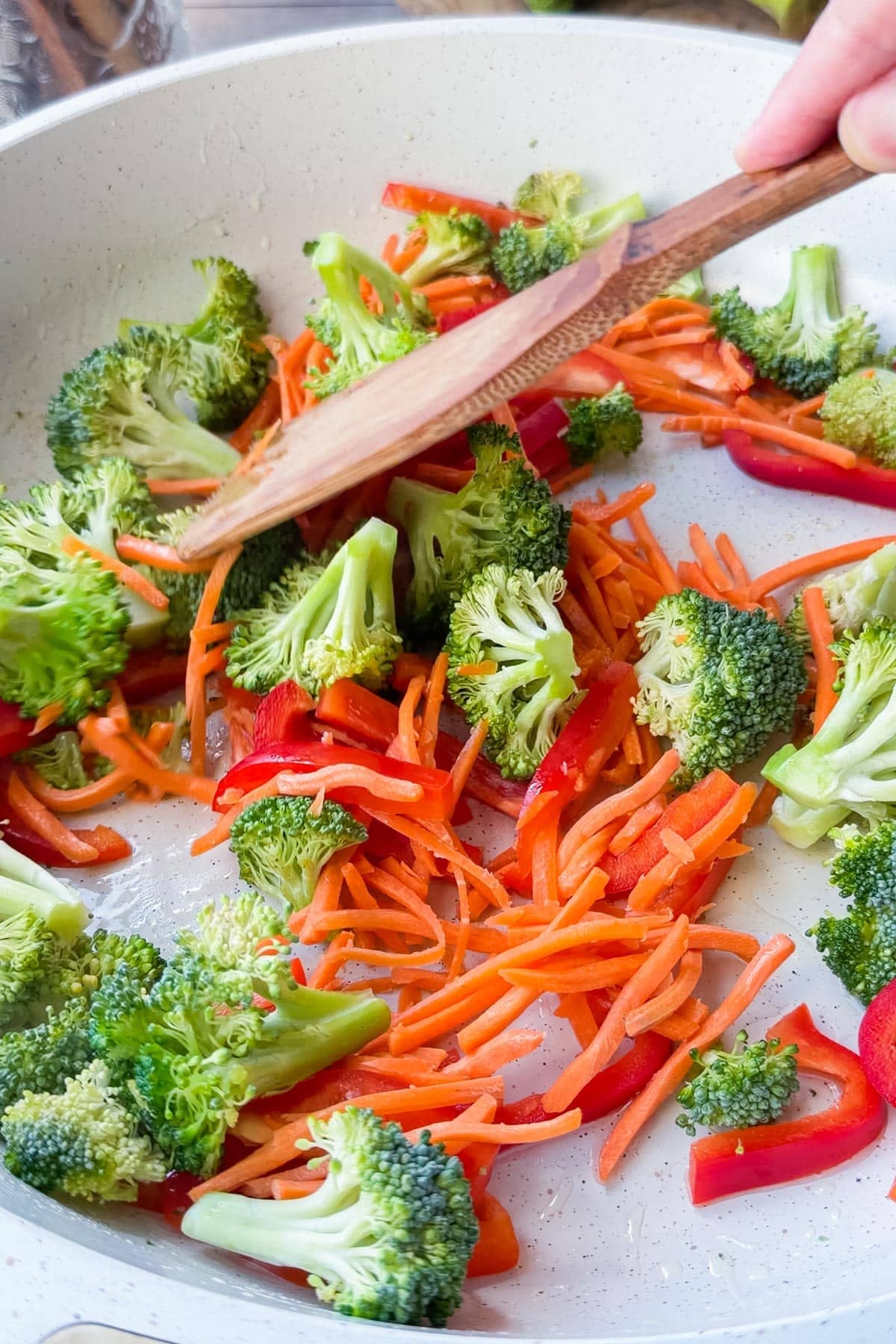 Broccoli florets, matchstick carrots, and red bell pepper cooking in a skillet for ground beef and broccoli