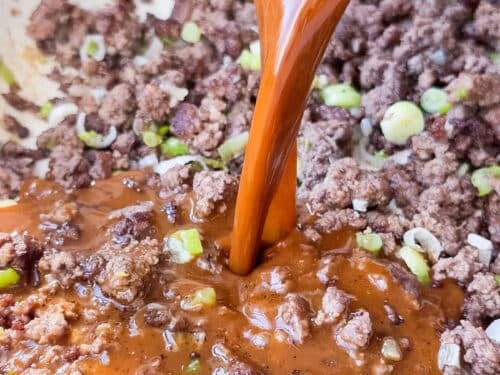 Soy-ginger stir fry sauce being poured over browned ground beef in a skillet
