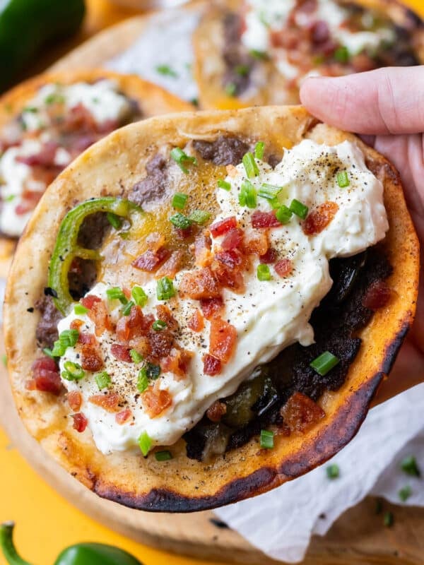 A hand holding a jalapeño popper smashed taco with whipped garlic cream cheese, bacon, and fresh jalapeños.