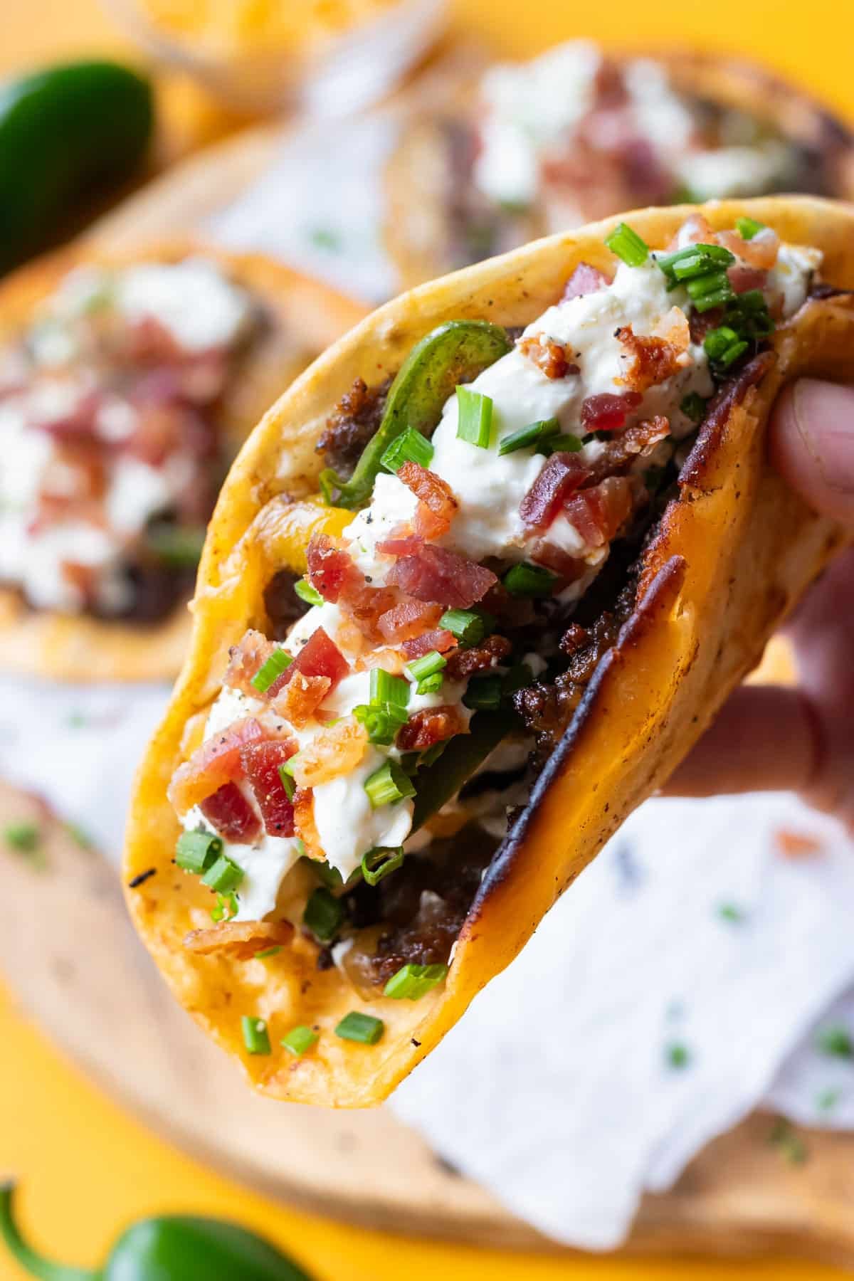 A hand holding a folded jalapeño popper smash taco with crispy beef and melted cheddar