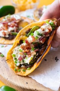 A hand holding a folded jalapeño popper smash taco with crispy beef and melted cheddar