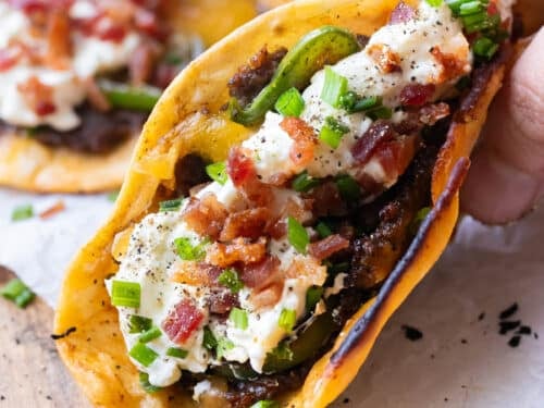 A hand holding a folded jalapeño popper smash taco with crispy beef and melted cheddar