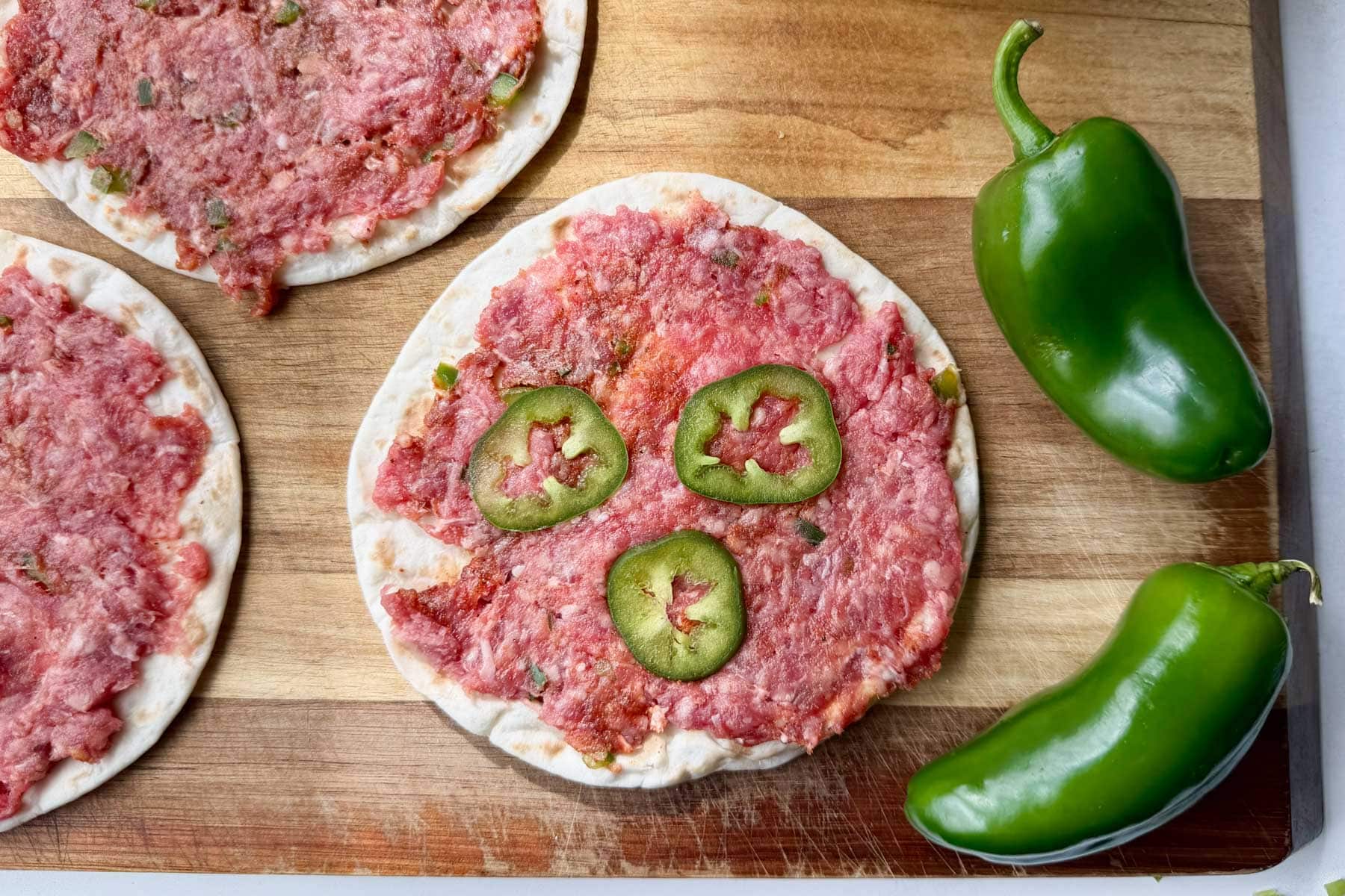 Seasoned beef pressed onto street taco tortillas with jalapeño slices for jalapeño popper tacos