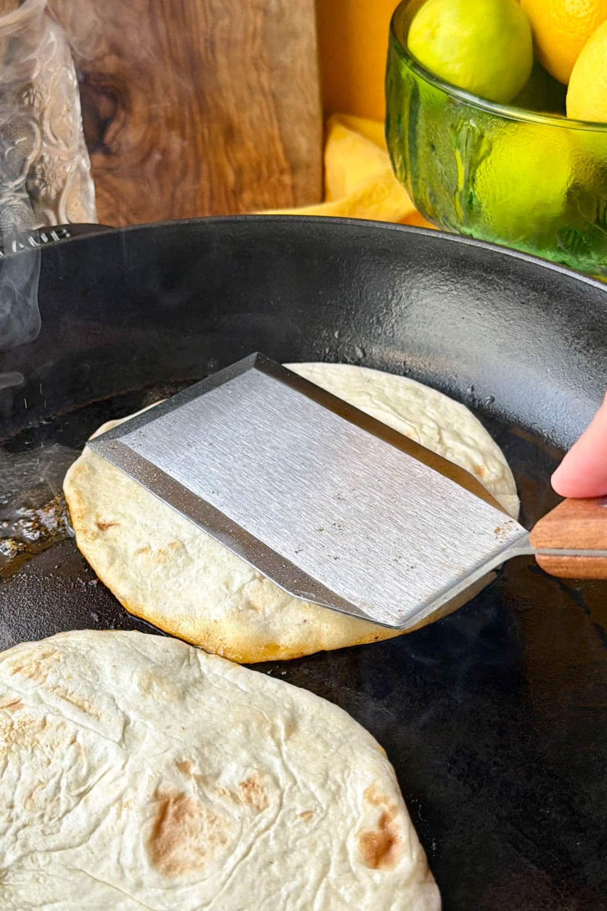 Pressing crispy beef tacos meat-side down in a cast iron skillet with a smash spatula